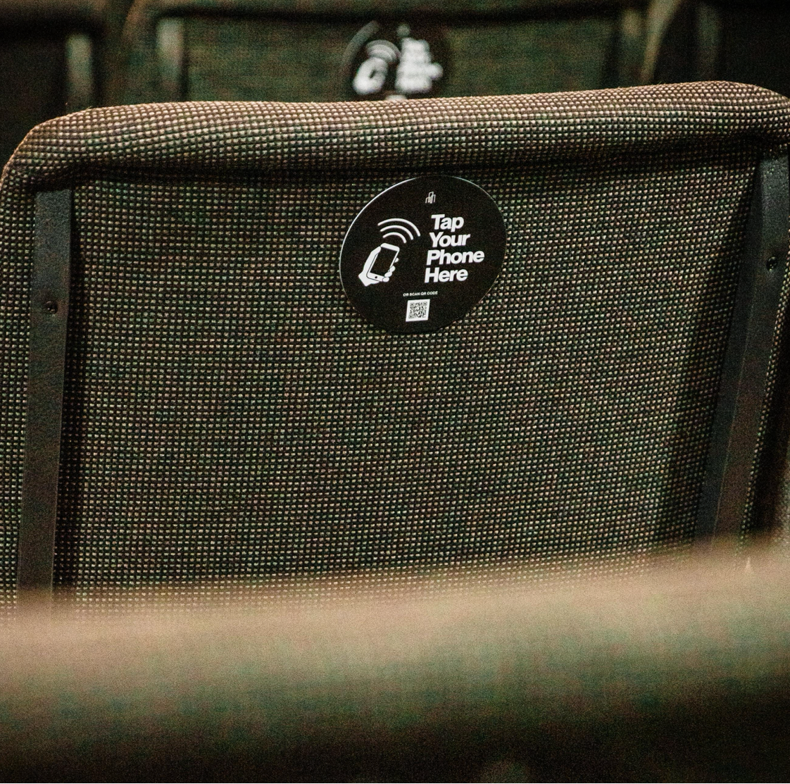 Row of theater seats with a 'Tap Your Phone Here' label on the backrest.